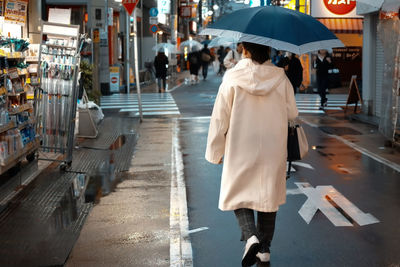 Rear view of woman walking on wet street in city