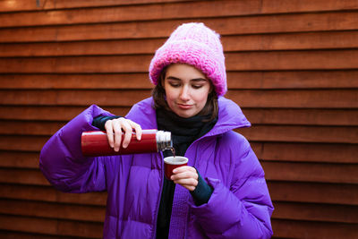 Young woman in winter clothes drinks hot tea from a thermos outdoors. winter