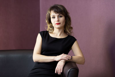 Portrait of beautiful young woman sitting against wall