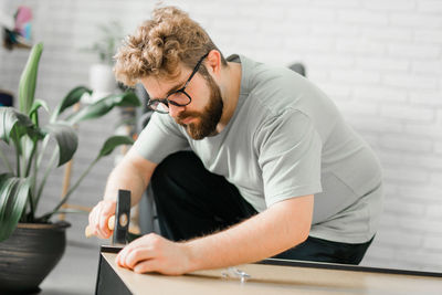 Side view of young man using mobile phone while sitting on table