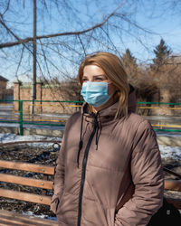 Young woman in a medical mask and jacket on a walk on a sunny day, mask mode, surgical mask