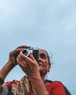 Low angle view of woman photographing against sky