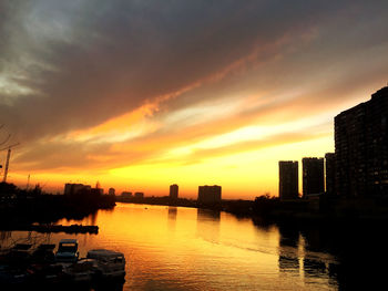 Silhouette buildings by river against sky during sunset