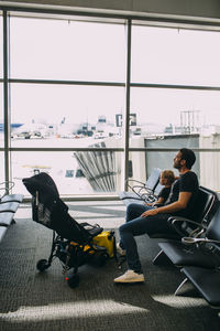 Side view of man using mobile phone while sitting on window