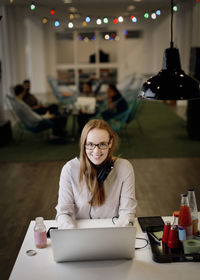 Portrait of smiling businesswoman working late on laptop in creative office