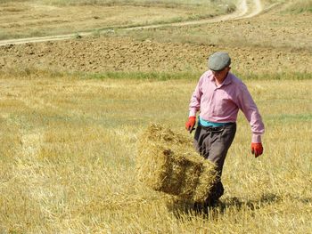 Man holding hay bale while walking on field