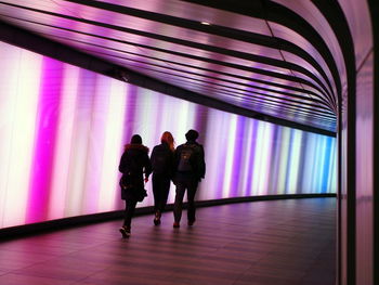 Rear view of people walking in illuminated building corridor