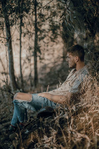 Side view of young man sitting on land in forest