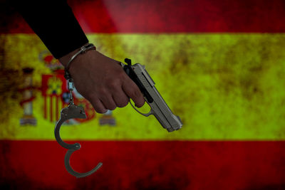 Cropped hand of male criminal holding gun against spanish flag