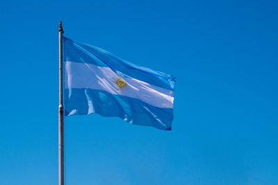 Low angle view of argentinian flag waving against clear blue sky