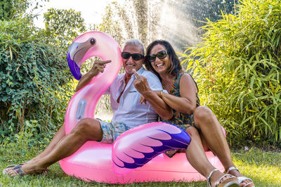 Beautiful smiling middle aged couple having fun sitting on pink flamingo inflatable toy