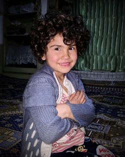 Portrait of smiling cute girl with arms crossed sitting at home