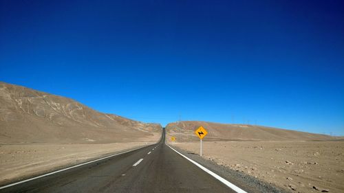 Road passing through desert against blue sky