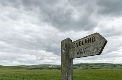 Low angle view of directional sign on green landscape against cloudy sky
