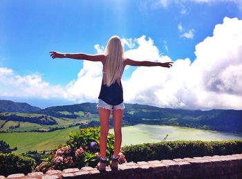 Rear view of girls with arms outstretched against clouds