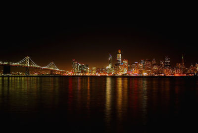 Illuminated buildings by river against sky at night