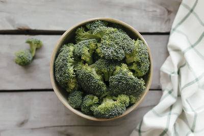 Green fresh broccoli in bowl on wooden background, white towel. healthy eating concept