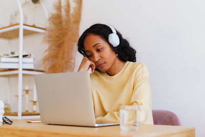 Bored and tired african-american female student watching online distance class on laptop