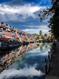 Canal by buildings in city against sky