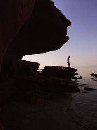 Side view of man standing on cliff by sea during sunset