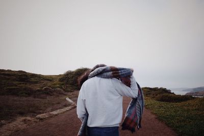 Rear view of woman with scarf walking on road against clear sky