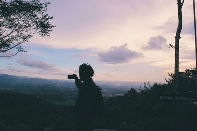 Silhouette woman photographing at sunset