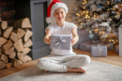 Full length of boy with gift box sitting by christmas tree