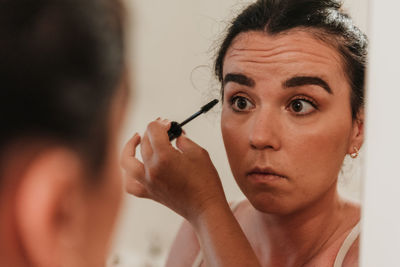 Mirror photo of beautiful young woman putting on makeup