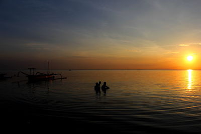 Silhouette people on sea against sky during sunset