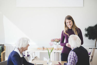 Granddaughter smiling while talking with grandparents sitting at table in nursing home