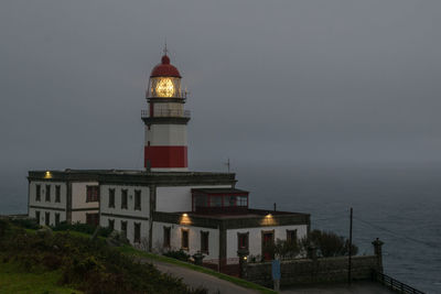 Lighthouse by building against sky at night