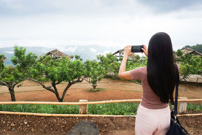 Rear view of woman photographing against sky