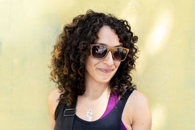 Mixed race woman with sunglasses standing against a yellow wall.