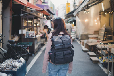 Rear view of woman with backpack standing on street in city