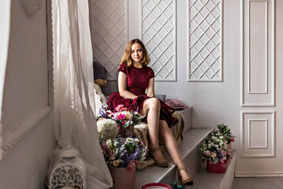 A cute stylish young girl in an elegant burgundy dress sits by the window in her room. teenager.