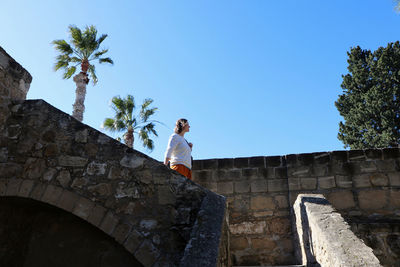 Low angle view of woman standing by built structure against sky