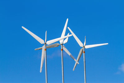 White wind turbines producing alternative energy on blue sky