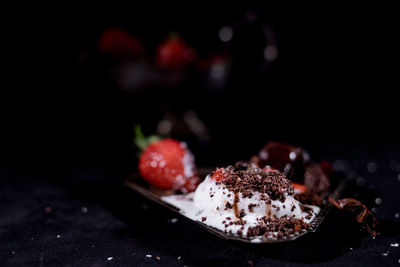 Close-up of strawberries with chocolate on table against black background