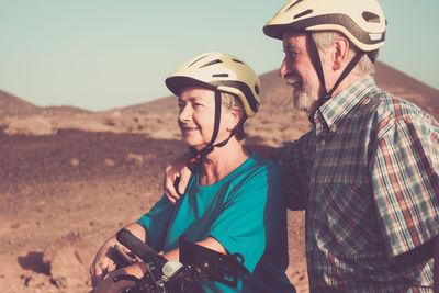 Smiling couple with bicycles wearing helmets standing on land 