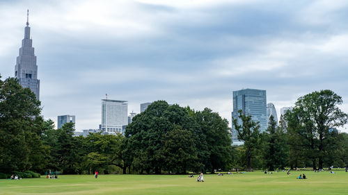 People in park by modern buildings against sky