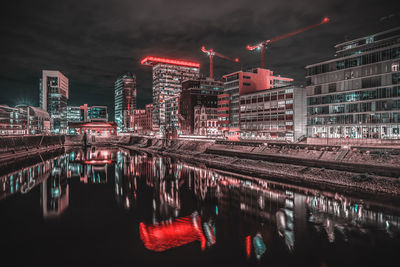 Illuminated buildings by river against sky at night