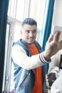 Young man taking selfie with mobile phone by window