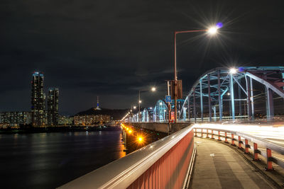 Illuminated bridge over river against sky at night