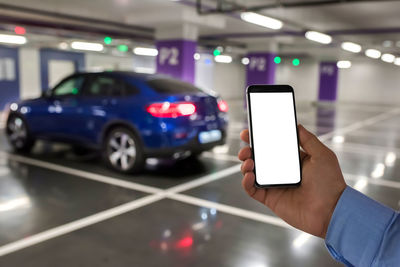 Smart phone with white screen in hand on car parking background