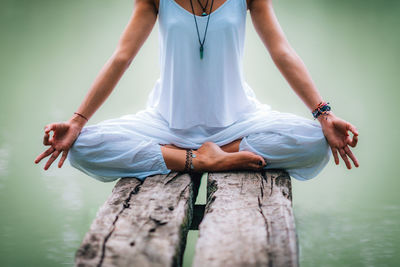 Midsection of woman doing yoga while sitting on pier at lake