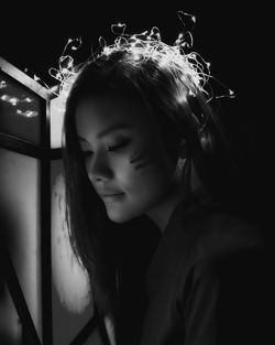 Close-up of woman wearing illuminated string lights in darkroom