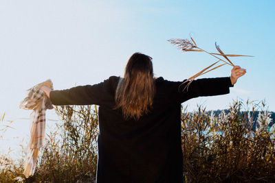 Rear view of woman with arms outstretched standing against plants