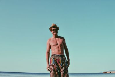 Shirtless man standing at beach against clear blue sky