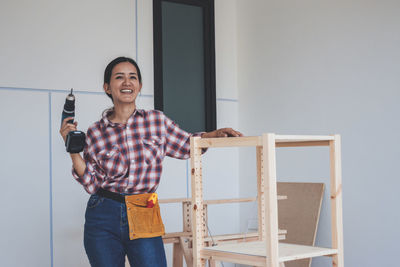 Portrait of smiling young woman standing against wall