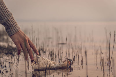 Close-up of person picking plastic bottle from lake during sunset